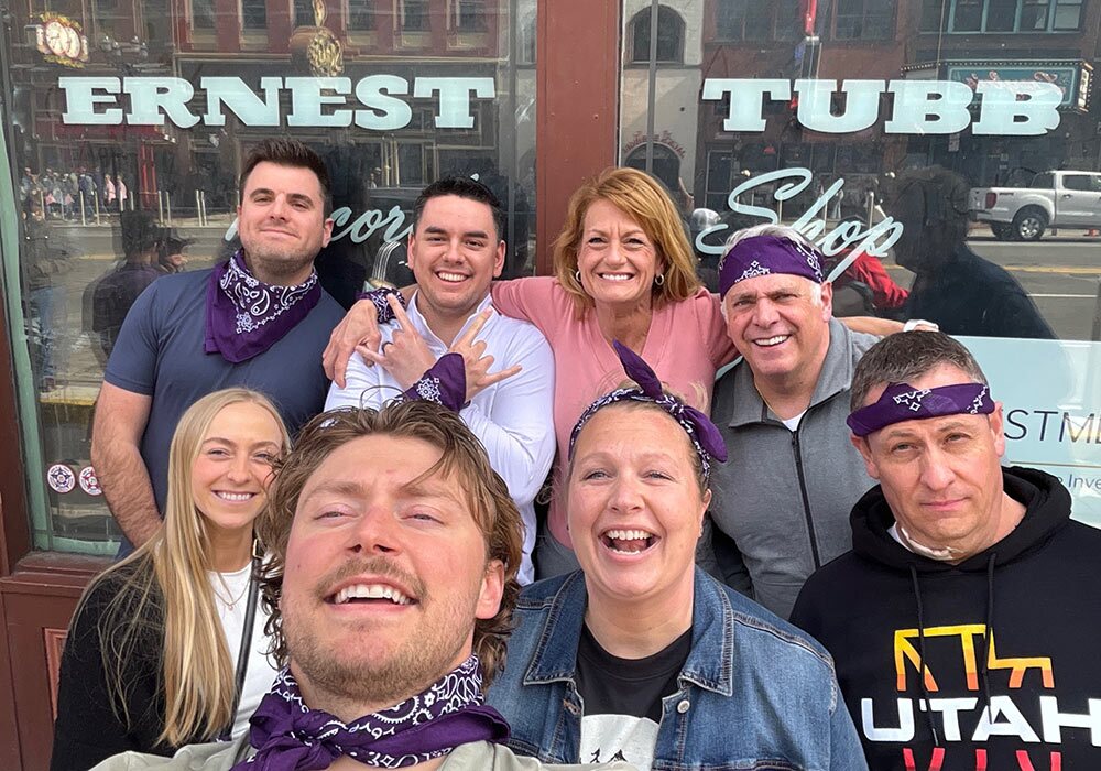 Group of people with matching purple bandanas posing for a selfie in front of the ernest tubb record shop.