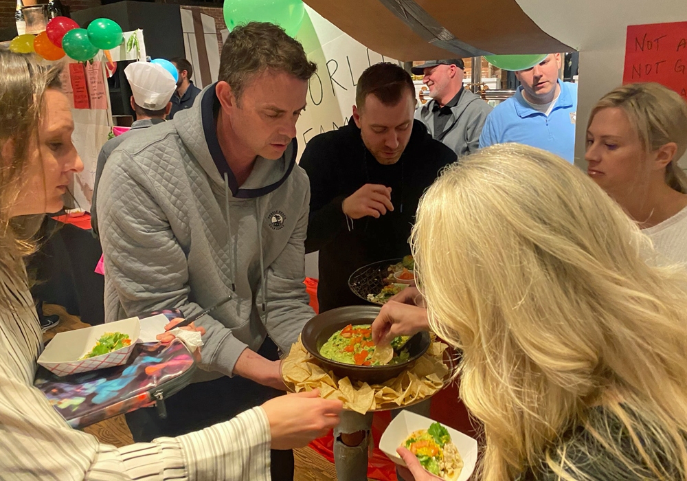 A group of people standing around a table eating food.
