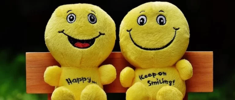 Two yellow stuffed animals sitting on a wooden bench.
