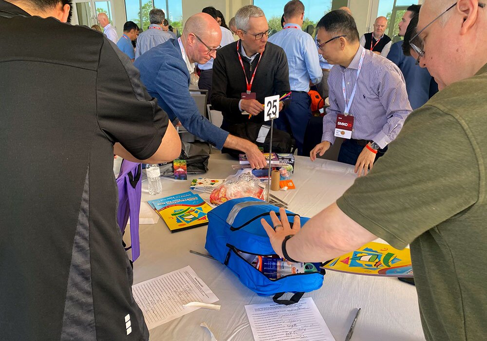 People gather around a table with snacks, papers, and a blue backpack during a meeting.