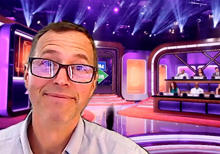 A man in glasses is standing in front of a television set.