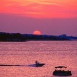 A boat in the water with the sun setting behind it.
