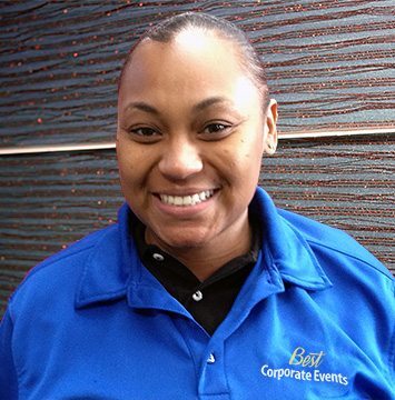 A woman in a blue shirt smiling in front of a wall.