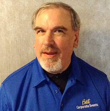 A man in a blue shirt standing in front of a wall.
