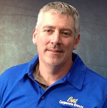 A man in a blue shirt standing in front of a wall.