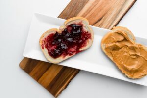 Two slices of bread on a rectangular white plate—one with peanut butter, the other with grape jelly—demonstrate how combining training and team building can create something even better together, arranged neatly on a wooden board.