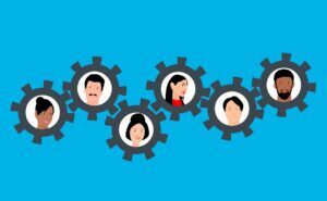 Illustration of six diverse people’s faces inside gears, symbolizing teamwork, collaboration, and accountability in the workplace, on a blue background.