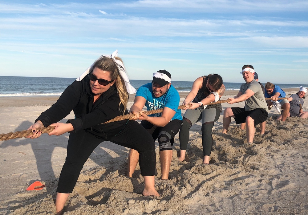 A group of people pulling a rope on the beach.