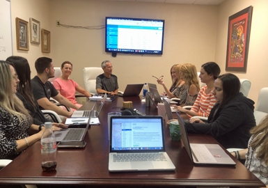 A group of people sitting around a table with laptops.