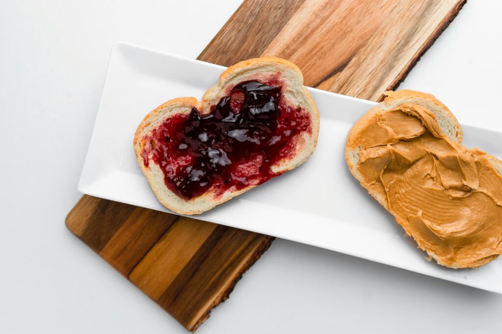 Two slices of bread on a rectangular white plate—one with peanut butter, the other with grape jelly—demonstrate how combining training and team building can create something even better together, arranged neatly on a wooden board.