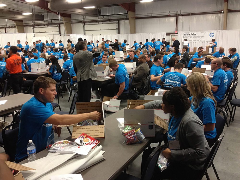 A group of people in blue shirts sitting at tables.