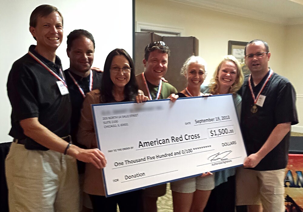 Group of individuals presenting a large $1,500 check to the american red cross.