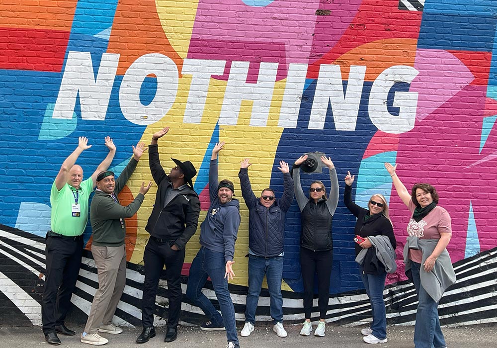 Group of people posing joyfully in front of a colorful mural that reads "nothing.