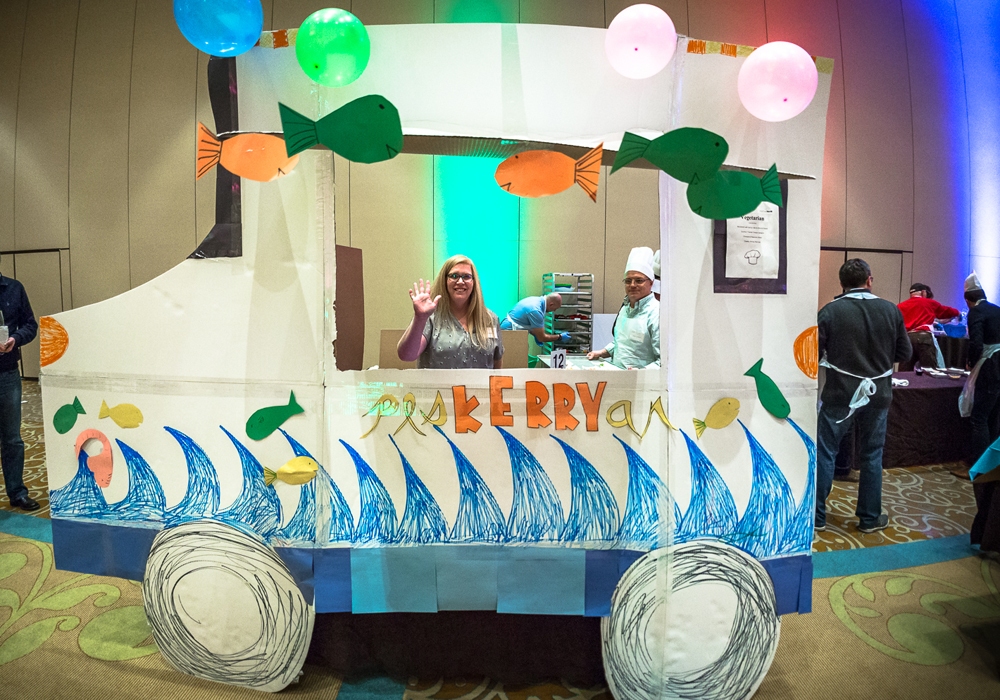 A woman is standing in front of a fish truck at a convention.