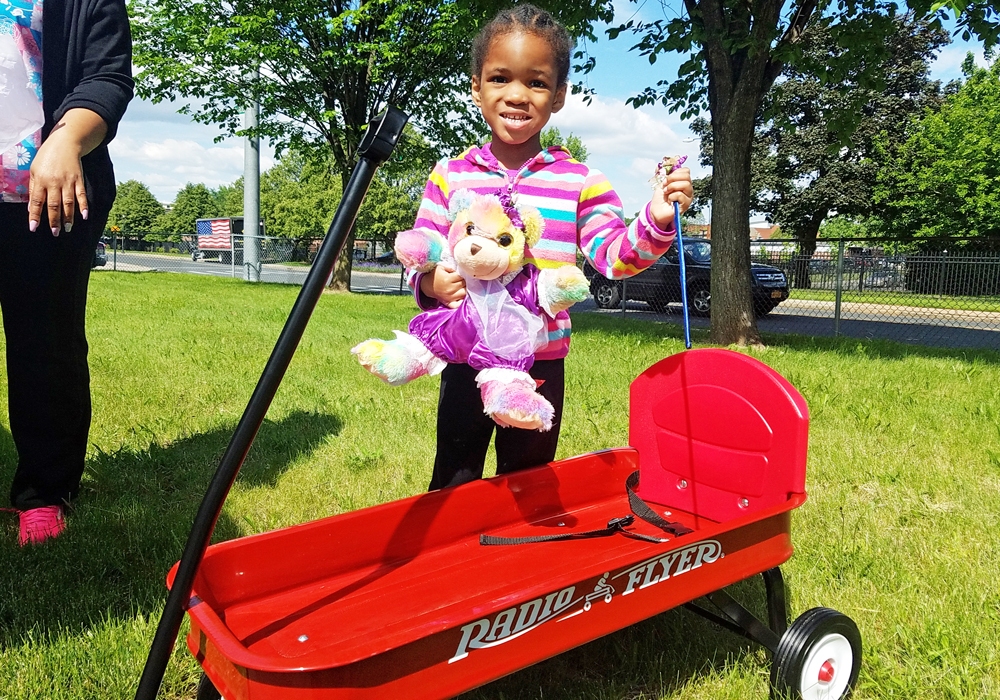 A young girl holding a teddy bear in a wagon.