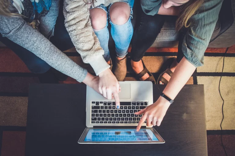 Three women engaged in team building activities, looking at a laptop on a coffee table.