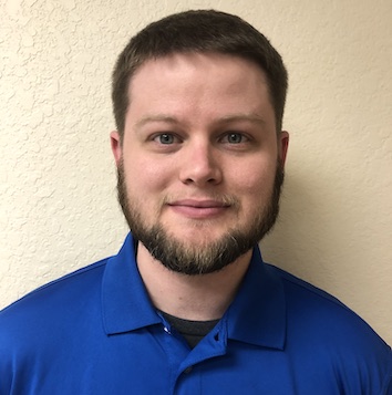 A man in a blue shirt standing in front of a wall.