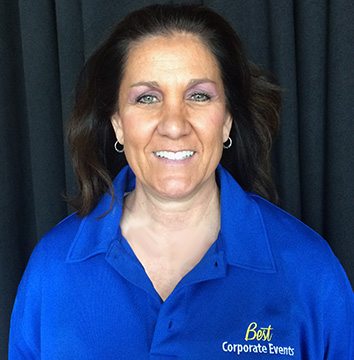 A woman in a blue shirt standing in front of a black curtain.