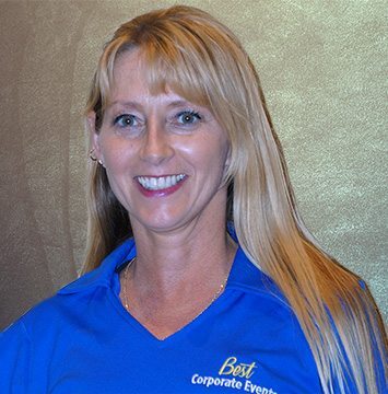 A woman in a blue shirt smiling in front of a wall.
