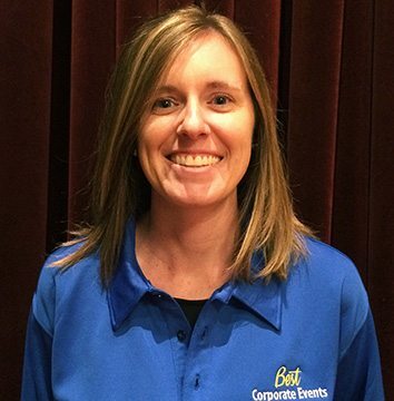 A woman in a blue shirt smiling in front of a curtain.