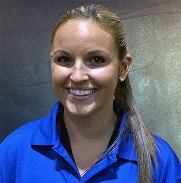A woman in a blue shirt smiling in front of a wall.