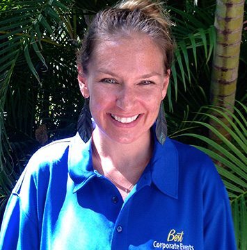 A woman in a blue shirt standing in front of palm trees.