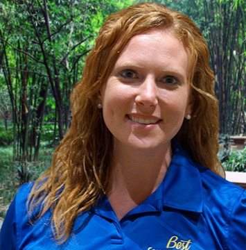 A woman in a blue shirt standing in front of a tree.