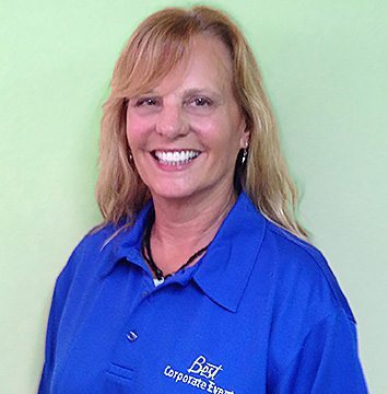 A woman in a blue shirt smiling in front of a green wall.