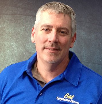 A man in a blue shirt standing in front of a wall.