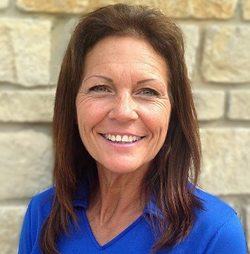 A woman in a blue shirt smiling in front of a stone wall.