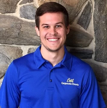 A young man in a blue shirt standing in front of a stone wall.