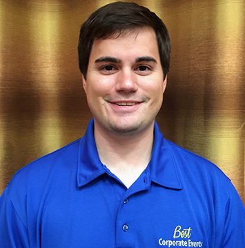 A man in a blue shirt standing in front of a curtain.