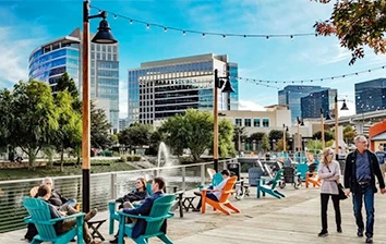A group of people are sitting on a boardwalk in front of a city.
