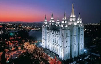 The salt lake temple is lit up at dusk in Utah.
