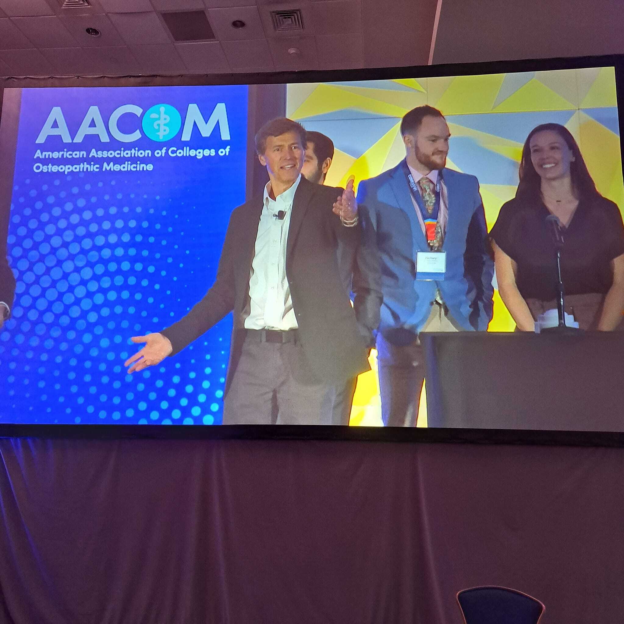 A group of people standing in front of a large screen.