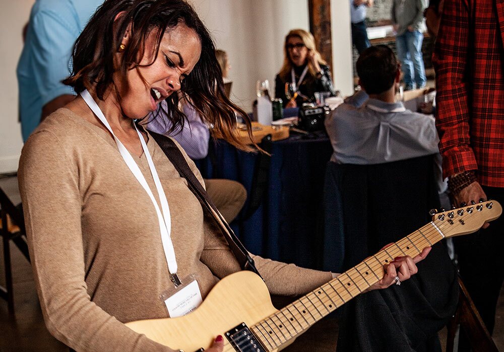 A woman playing an electric guitar in a room full of people.