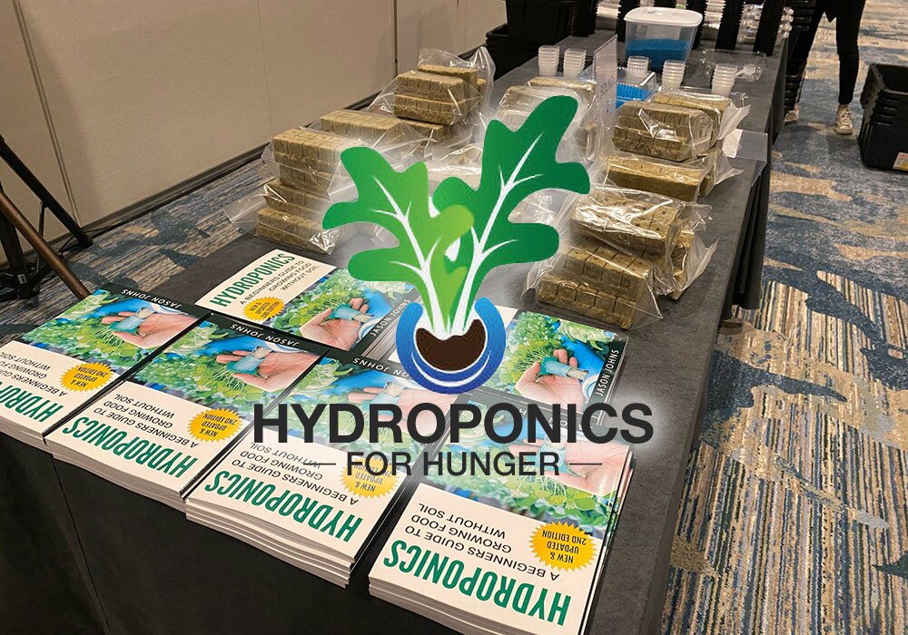 Table with stacks of books titled "Hydroponics for Hunger" and hydroponic supplies, including plant starter cubes and nutrient solutions, set for a generous hydroponics donation to support sustainable farming initiatives.