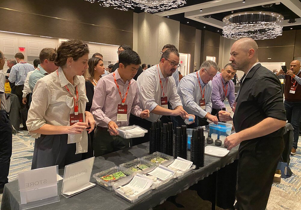 A group of people eagerly line up to receive boxed meals from a server at the conference, where a portion of the ingredients come from local hydroponics gardens, thanks to a generous donation.