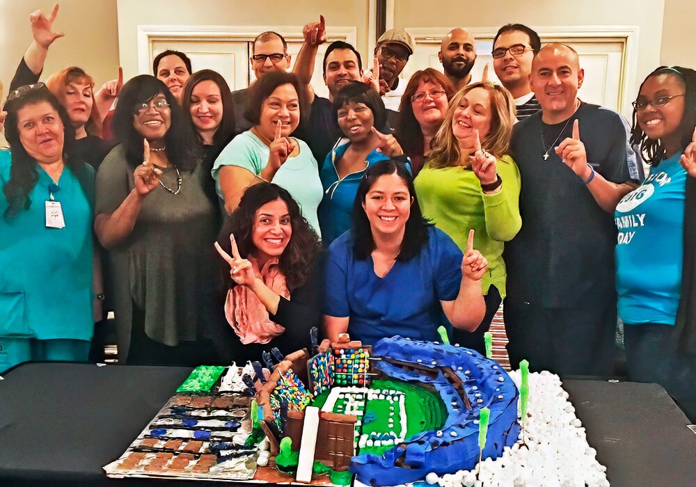 A group of people posing in front of a cake.