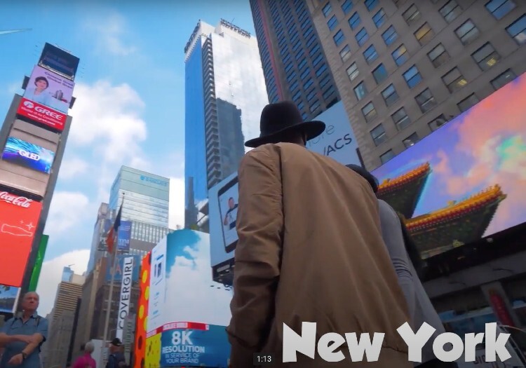 A man in a hat is walking down a street in times square.
