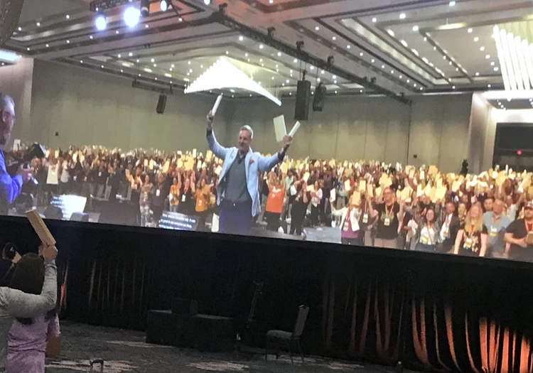 A large screen showing a group of people raising their hands in the air.