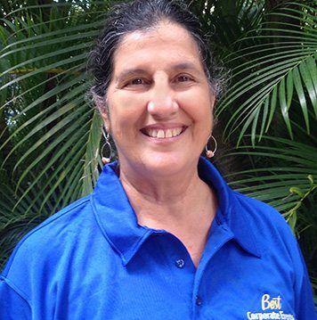 A woman in a blue shirt smiling in front of palm trees.