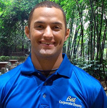 A man in a blue polo smiles in front of a bamboo forest.