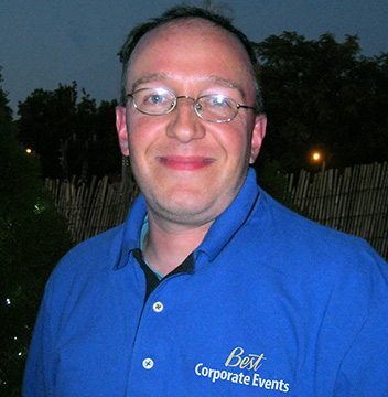 A man in a blue shirt standing in front of a tree.
