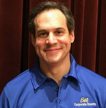 A man in a blue shirt smiling in front of a curtain.