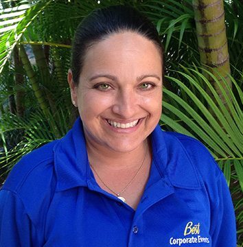 A woman in a blue shirt smiling in front of palm trees.
