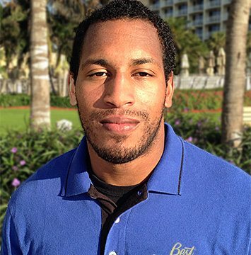 A man in a blue shirt standing in front of palm trees.