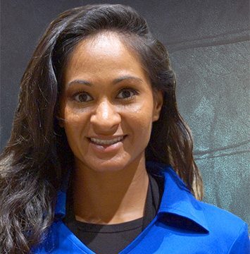 A woman in a blue shirt smiling in front of a chalkboard.
