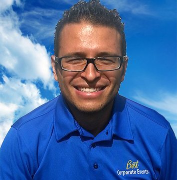 A man in a blue shirt smiling in front of a blue sky.