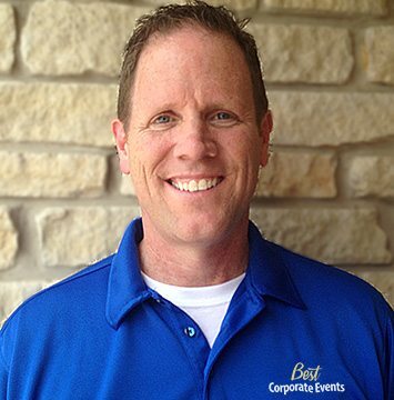 A man in a blue shirt smiling in front of a stone wall.